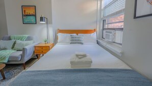 Ein ordentlich eingerichtetes Schlafzimmer mit Bett, Nachttisch, Lampe und einem gerahmten Bild an der Wand.