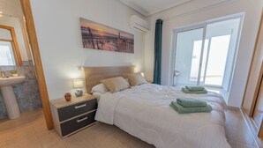 Une chambre à coucher moderne avec un grand lit, une table de chevet, un climatiseur fixé au mur et une fenêtre avec des rideaux.