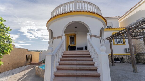 Un escalier menant à une entrée abritée, dotée d’une porte jaune, de balustrades blanches et d’un espace piscine.