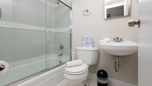 A bathroom with a glass-enclosed shower, a toilet, a sink, and a trash bin. - Cozy Loft in South End (Boston)