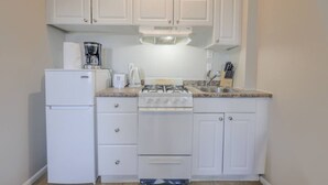 A compact kitchen with white cabinets, a refrigerator, a stove, and a coffee maker. - Chic South End Studio | Perfect for Nurses! (Boston)