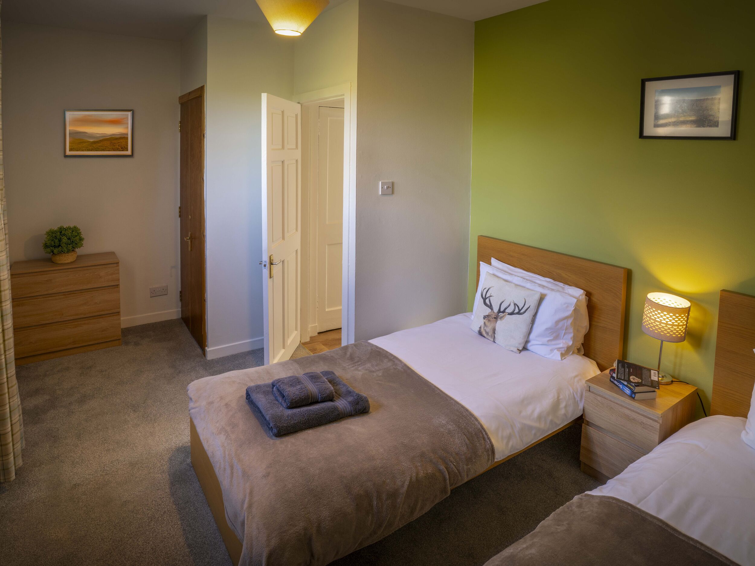 A bedroom with two beds, a dresser, a bedside lamp, and a door leading to another room.