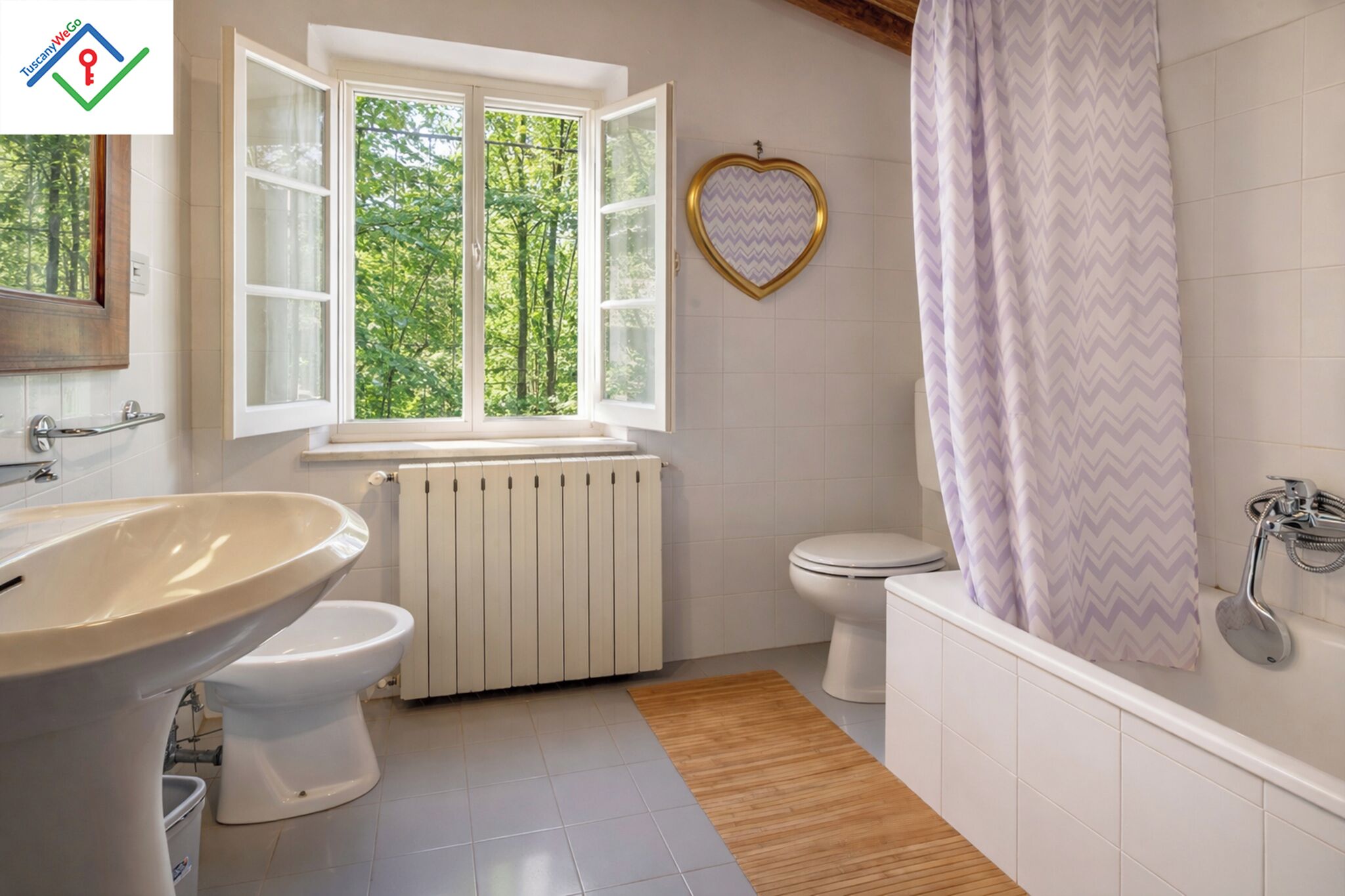 A bathroom with a window, a radiator, a toilet, a bathtub, and a sink.
