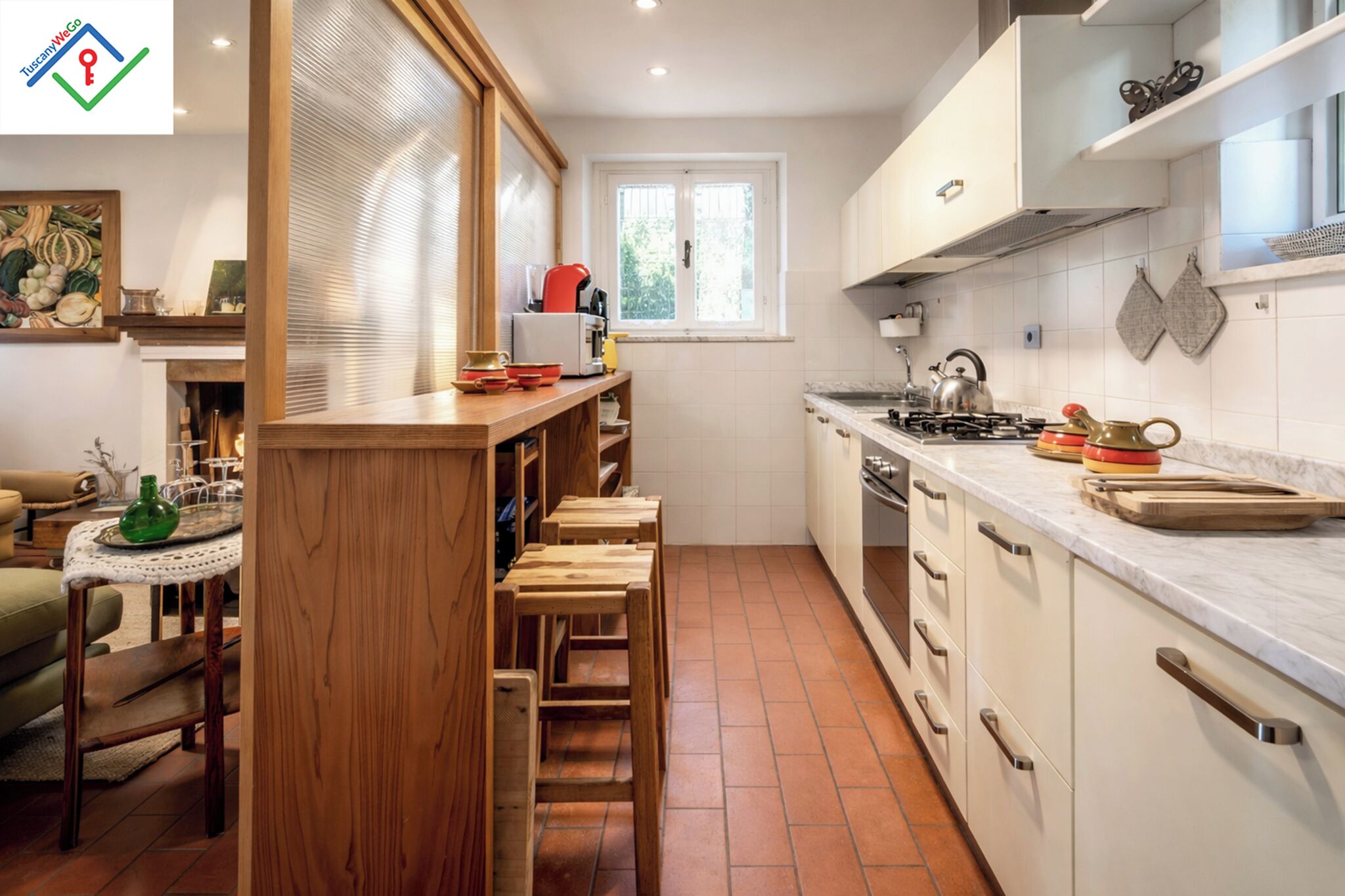 Una cocina compacta con una isla central, armarios blancos y un ventanal que proporciona luz natural.