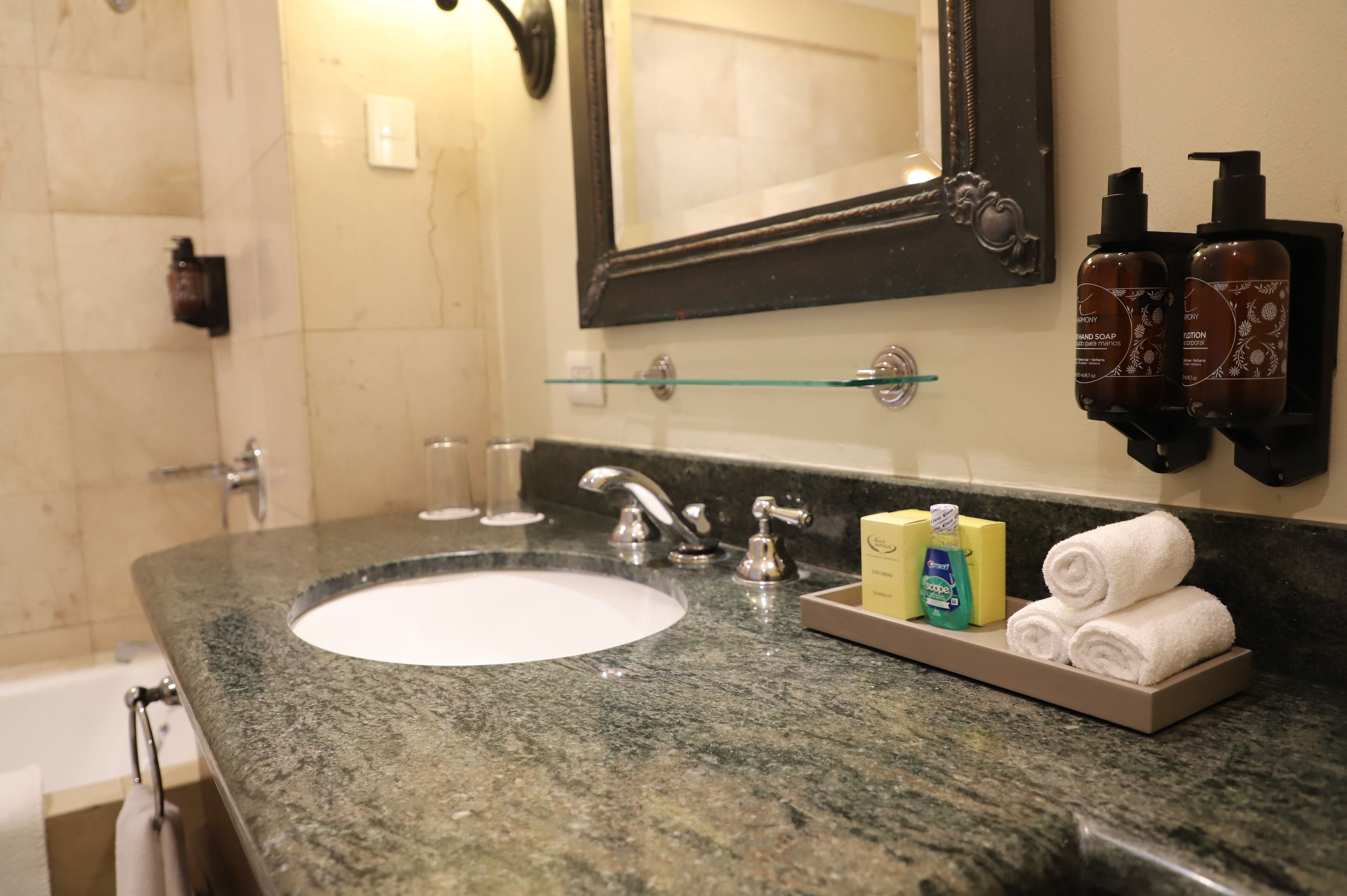 A bathroom with a granite countertop, a white sink, a mirror, and toiletries.