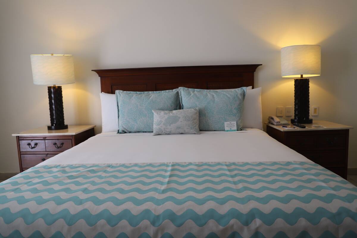 A neatly made bed with a patterned bedspread, two bedside lamps, and a wooden headboard.