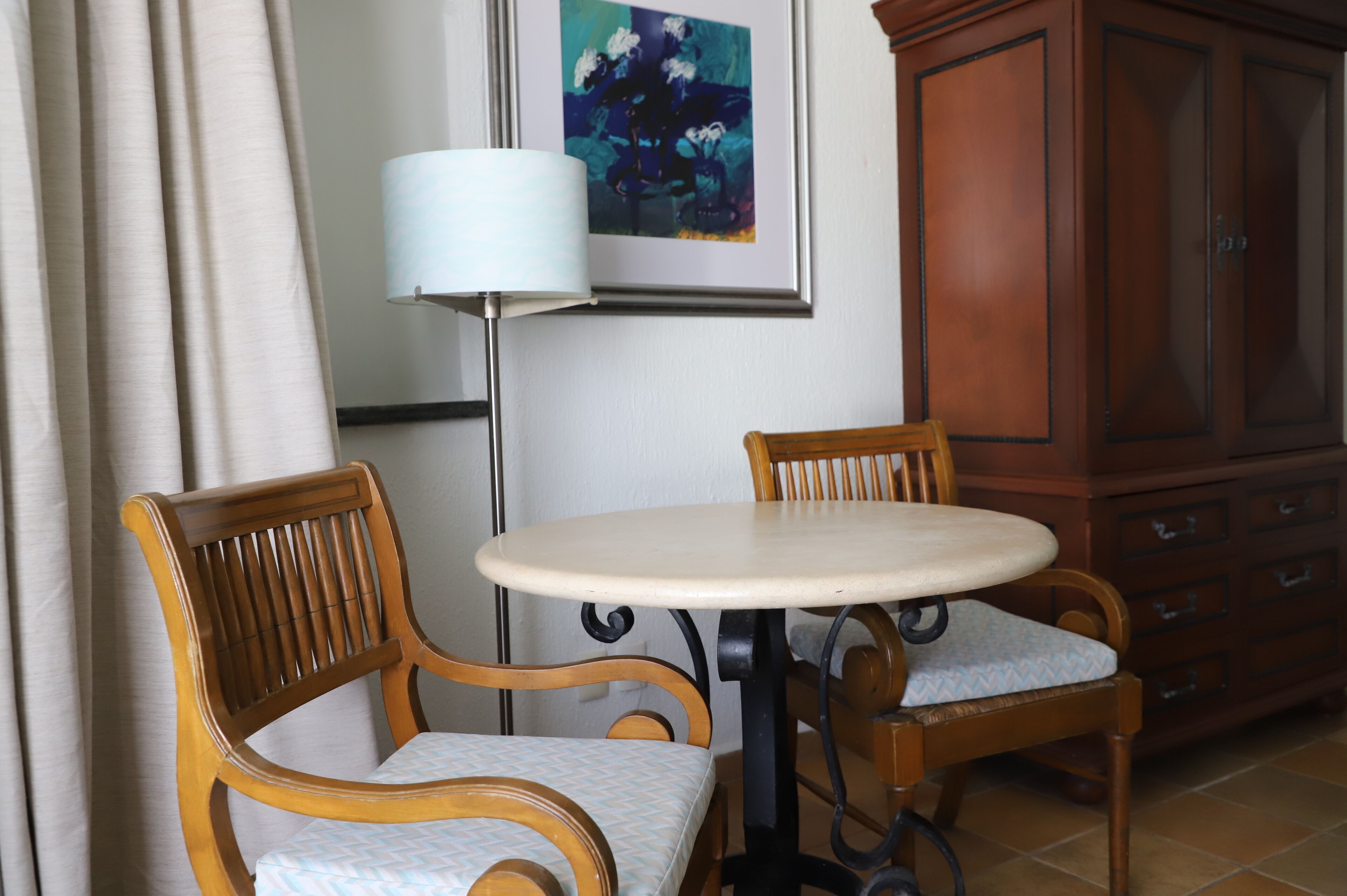 Una habitación con dos sillas de madera, una mesa redonda, una lámpara y un armario.