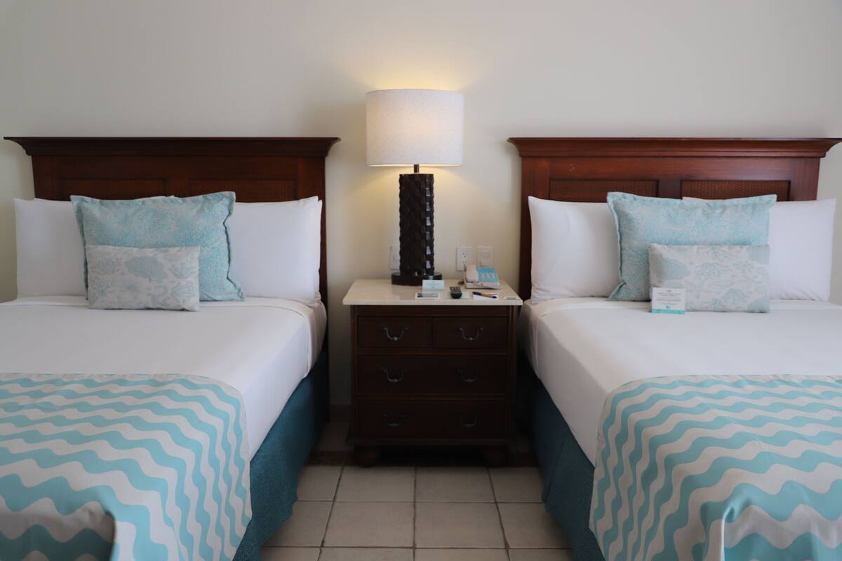 A hotel room with two beds, each with a patterned bedspread, a nightstand with a lamp, and a dresser with drawers.