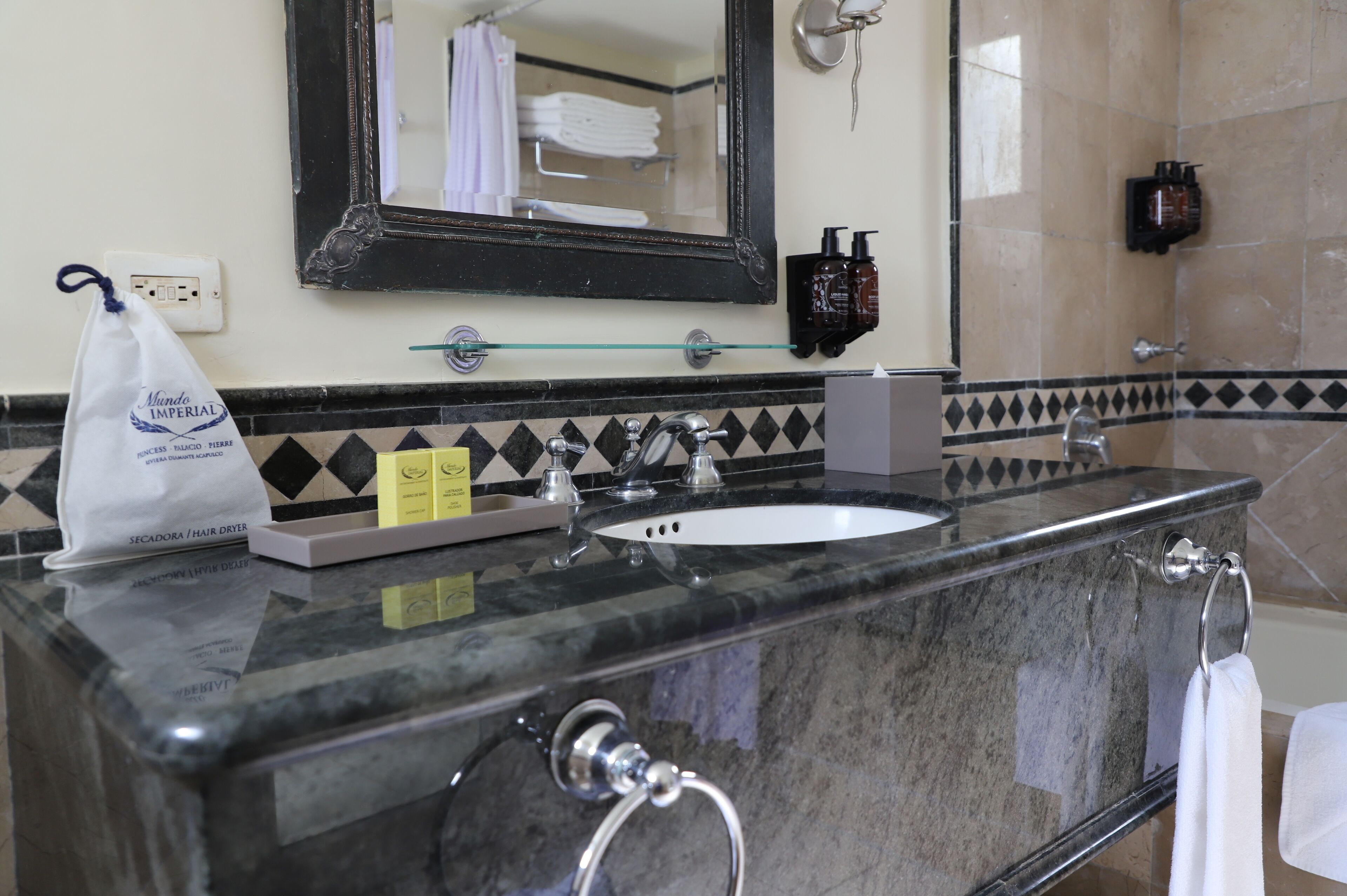 Un baño con un lavamanos de mármol, repisa de vidrio, espejo y toallero.