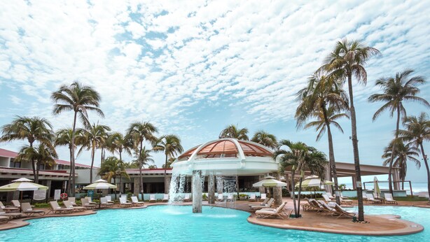 A resort pool area with lounge chairs, palm trees, and a water fountain. - Pierre Mundo Imperial All Inclusive  (Acapulco)