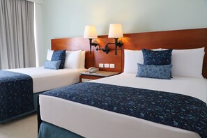 Een hotelkamer met twee bedden, elk met een blauwe bloemenprint sprei, witte kussens en een houten hoofdbord. Twee wandlampen zijn bevestigd aan het hoofdbord, en er staat een nachtkastje met een telefoon en een lamp bij.