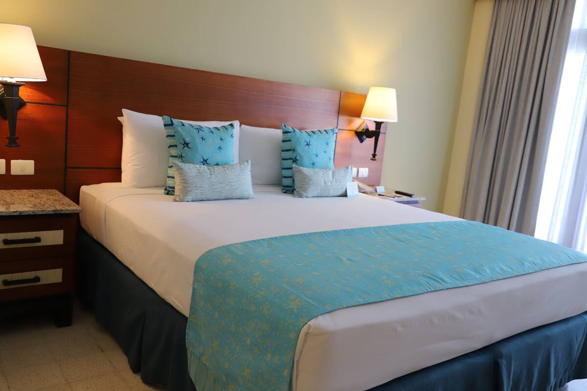 A hotel room with a large bed, two bedside lamps, a wooden headboard, and a nightstand with drawers.