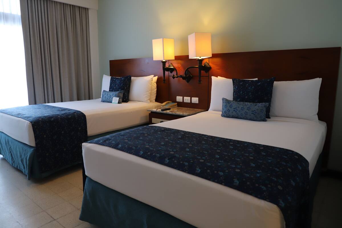 Two double beds with matching headboards and nightstands, each with a lamp and a telephone.
