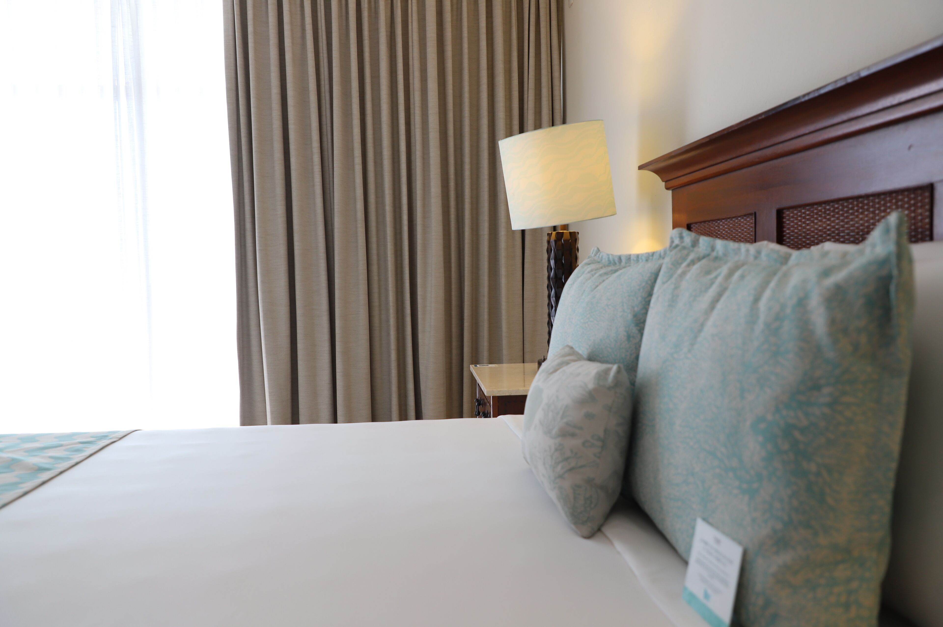 Habitación de hotel con una cama grande, una mesita de noche con lámpara y vistas a las cortinas.