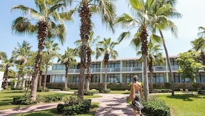 A pathway lined with palm trees leading to a building with a modern design and large windows. - Pierre Mundo Imperial All Inclusive  (Acapulco)