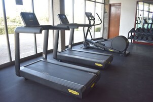 Un gimnasio con cintas de correr, una bicicleta estática y un estante con mancuernas.
