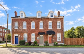 A two-story brick building with a blue door, a green door, and a black awning over the front entrance.