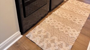 Uma lavanderia compacta e escura, com uma máquina de lavar e uma secadora pequenas, uma cesta de roupa branca sobre a secadora e um tapete bege estampado no chão.