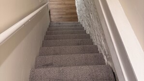 Escadaria revestida com carpete, parede texturizada em um lado e piso de madeira no topo.