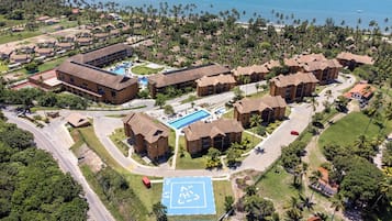 An aerial view of a resort with multiple bungalow-style buildings, a central pool area, and a beachfront.
