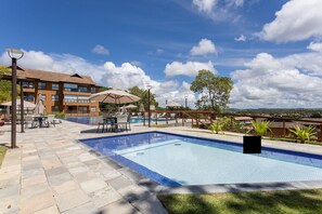 Una piscina con sillas de descanso y sombrillas, rodeada por un patio de piedra y un edificio con varias ventanas.