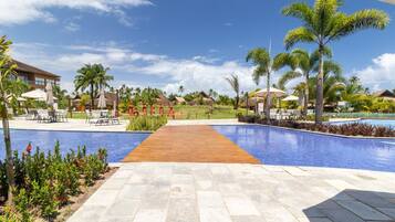 A resort pool area with a wooden walkway, palm trees, and lounge chairs.