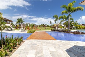 A resort pool area with a wooden walkway, palm trees, and lounge chairs. - Eco Resort Praia dos Carneiros Luxury Apt (Praia dos Carneiros)