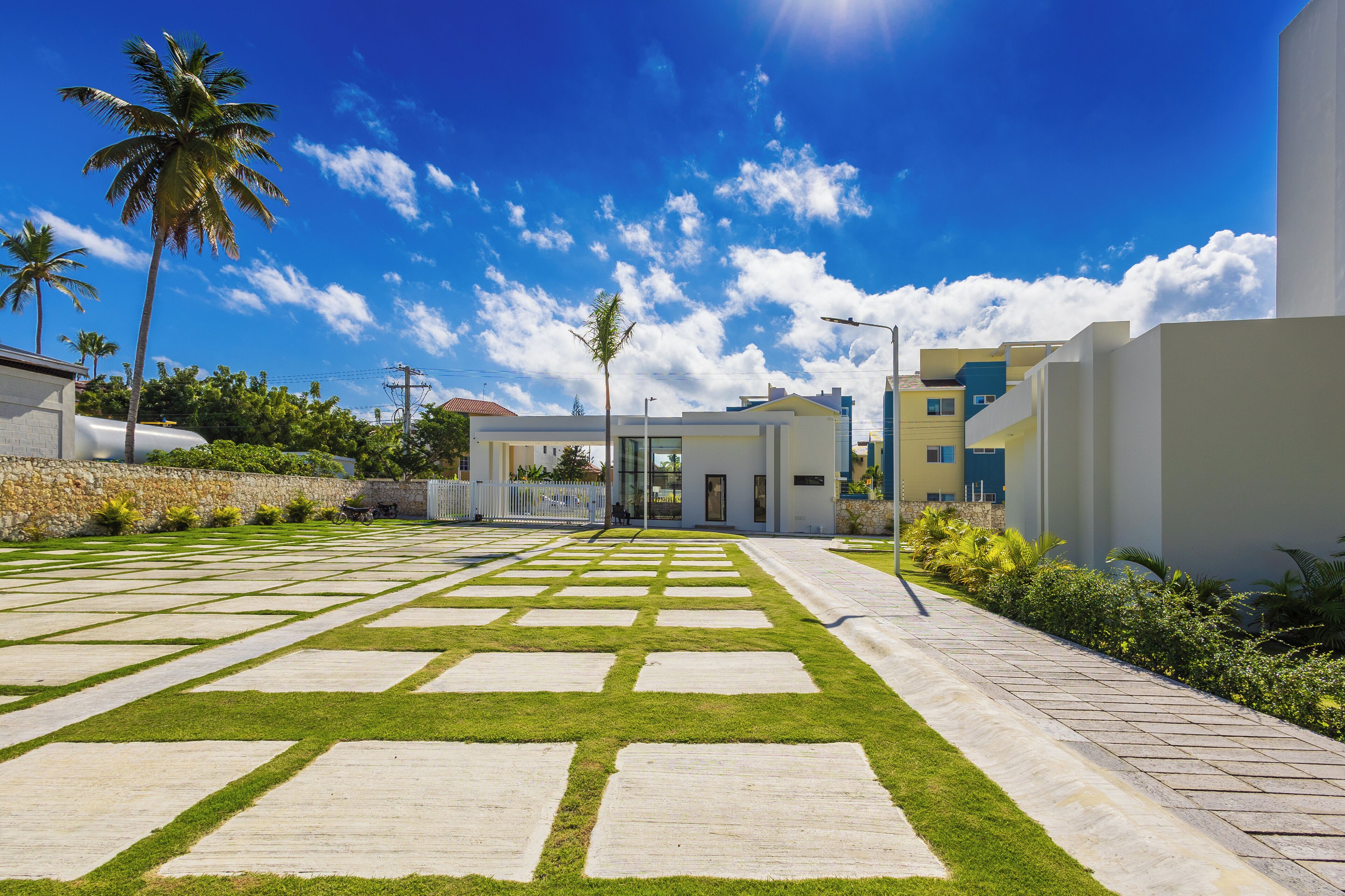 Un edificio moderno con un patio empedrado, palmeras y un cielo azul despejado.