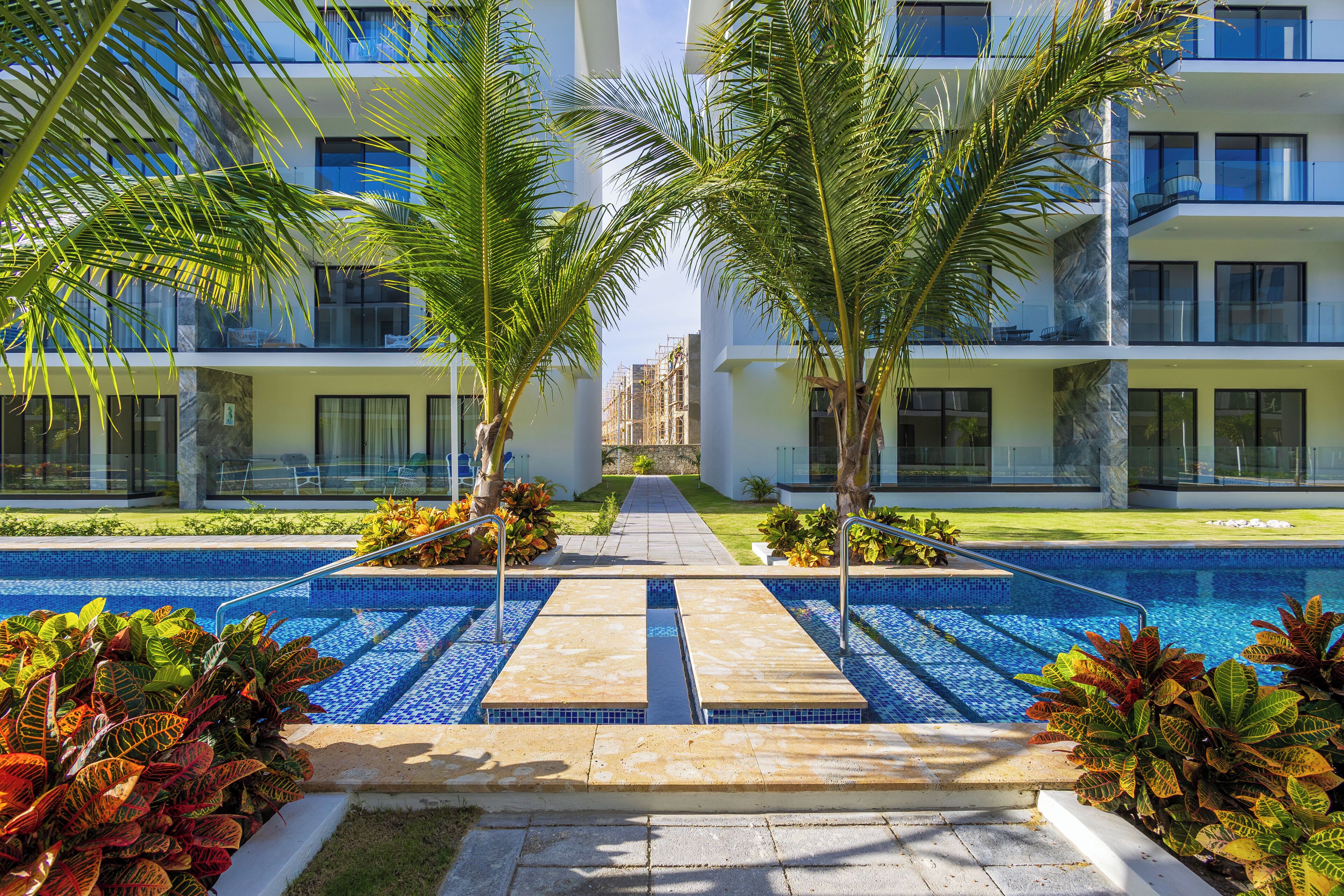 A modern hotel with a pool, palm trees, and a clear view of the building's architecture.