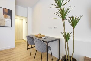 Un comedor moderno con una mesa de madera oscura, dos sillas tapizadas en gris y una planta en maceta con hojas altas y delgadas.