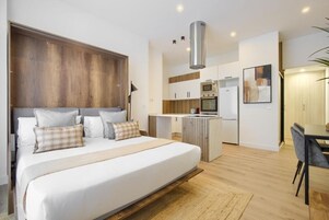 Un dormitorio moderno con una cama grande, un cabecero de madera y una kitchenette al fondo.