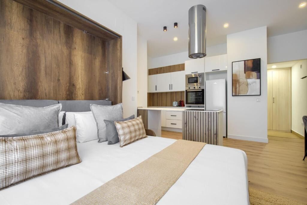 Un dormitorio moderno con una cama grande, un cabecero de madera y una kitchenette al fondo.
