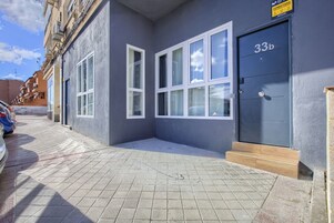 Un edificio con fachada gris, número 33b, con ventanas grandes y una puerta azul oscuro.