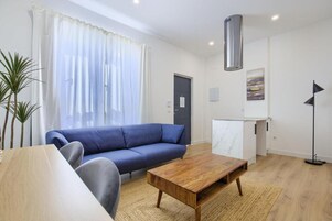 Un salón moderno con un sofá azul, una mesa de centro de madera y una zona de cocina con un armario blanco.