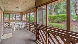 A covered outdoor area with a wooden railing, a carpeted floor, and a view of greenery outside. - Heron Pointe D2- 2BR/2BA- Pool, Hot Tub (Myrtle Beach)