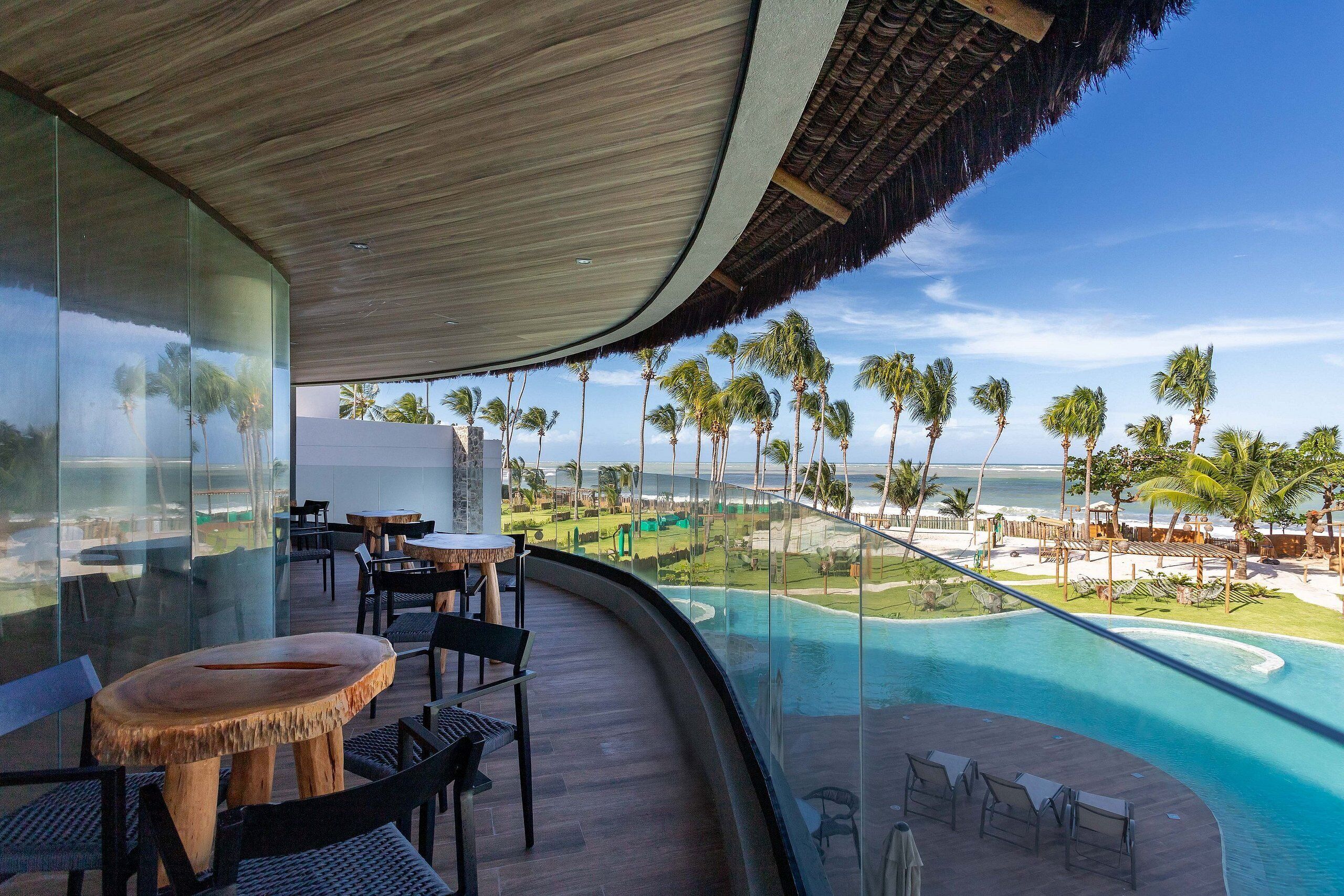 A modern resort with a curved balcony overlooking a pool and beach.