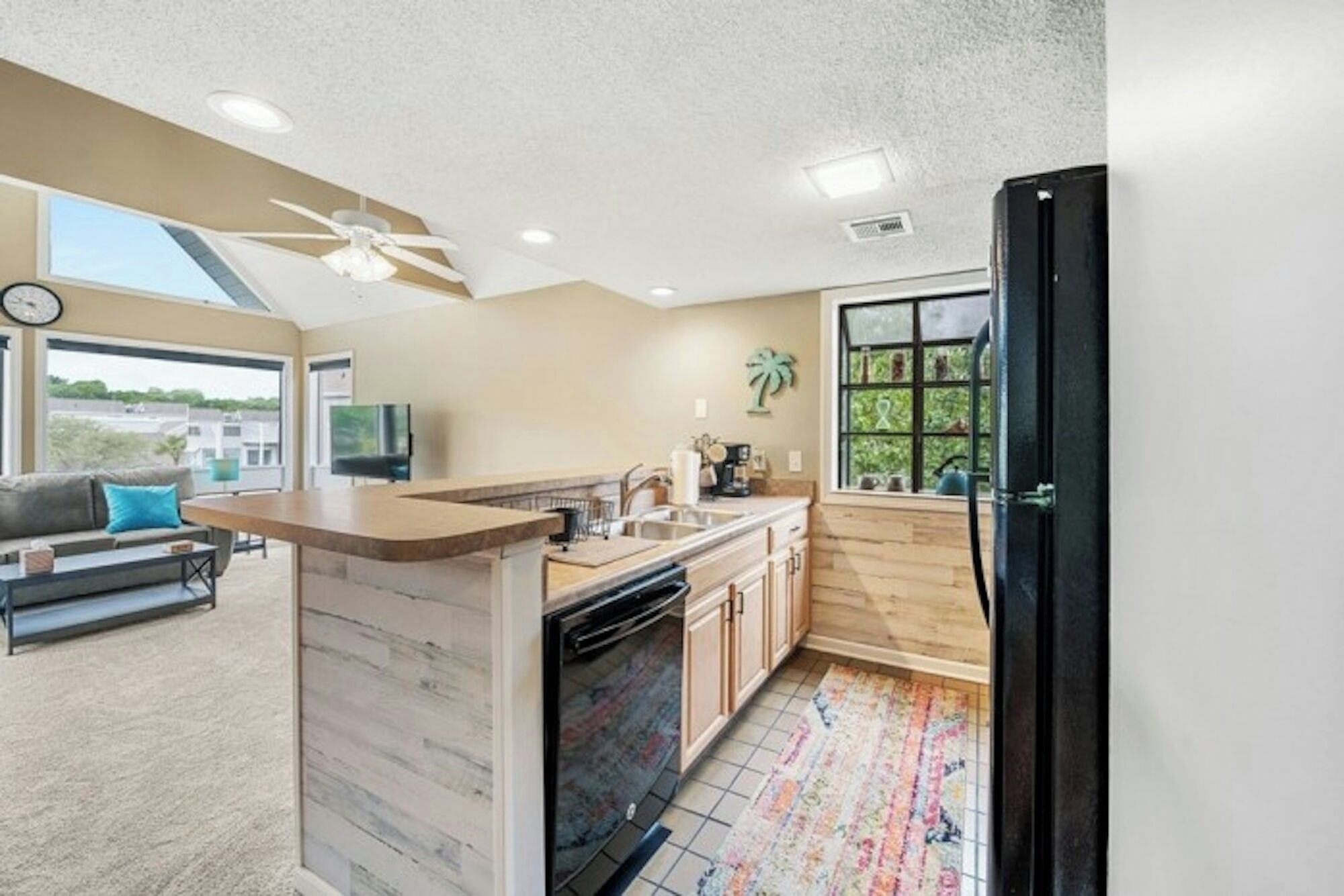 A modern kitchen with a wooden island, a large window, and a view of greenery outside.