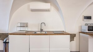 Une cuisine compacte équipée d’un évier intégré, d’un four à micro-ondes et d’un climatiseur fixé au mur.