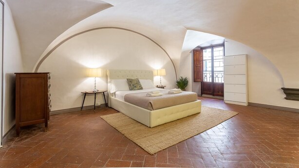 Une chambre à coucher comprenant un lit, deux tables de chevet, une commode, un meuble en bois et une grande fenêtre en arc de cercle.