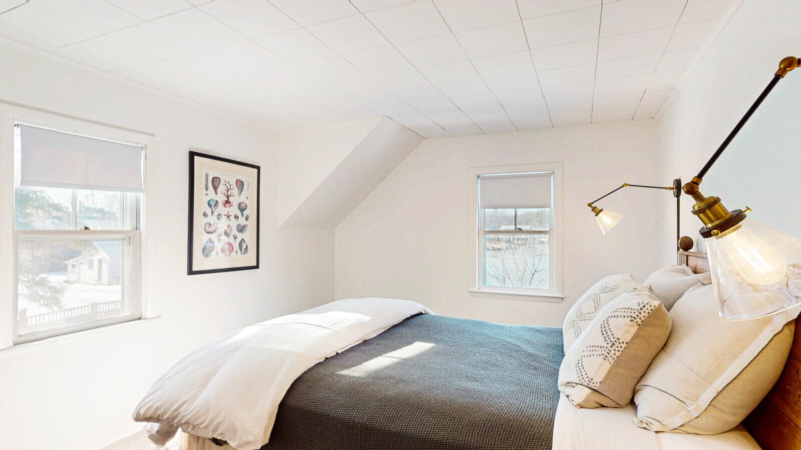A bedroom with a bed, a framed picture, a window, and a lamp.