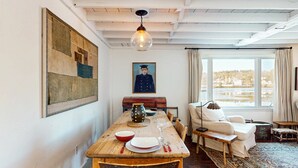 Una sala de estar acogedora con una mesa de comedor de madera dispuesta para dos personas, un sofá cómodo y un gran ventanal con vistas a un lago.