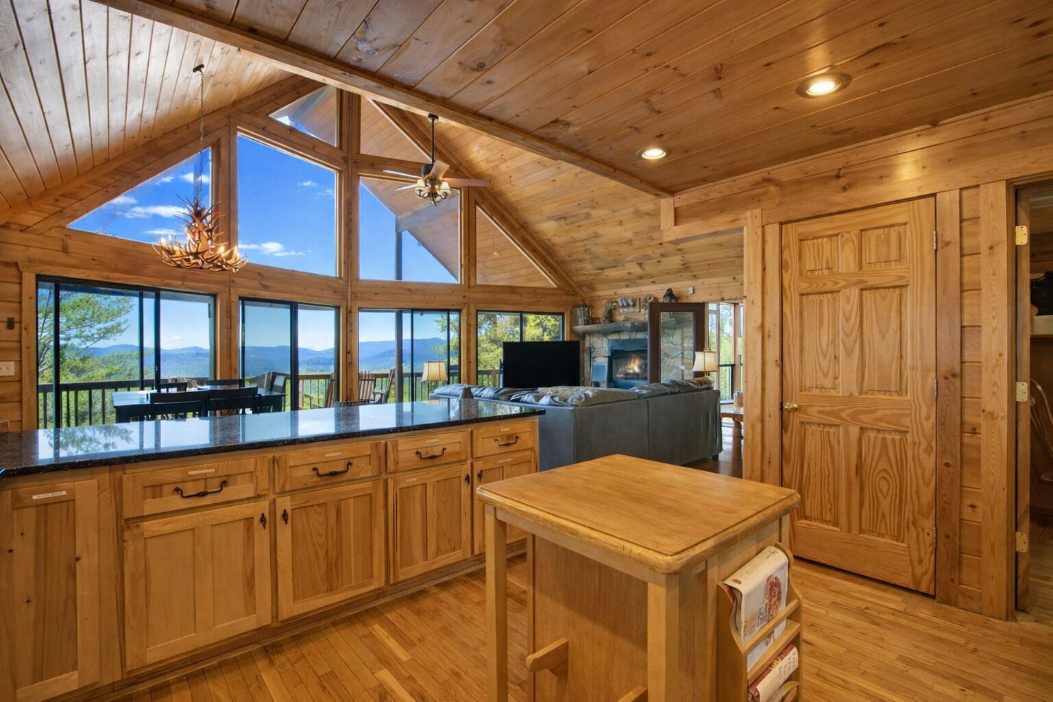 A spacious kitchen with large windows, a stone fireplace, and a wooden ceiling.