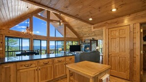 Une cuisine spacieuse, dotée de grandes fenêtres, d’une cheminée en pierre et d’un plafond en bois.