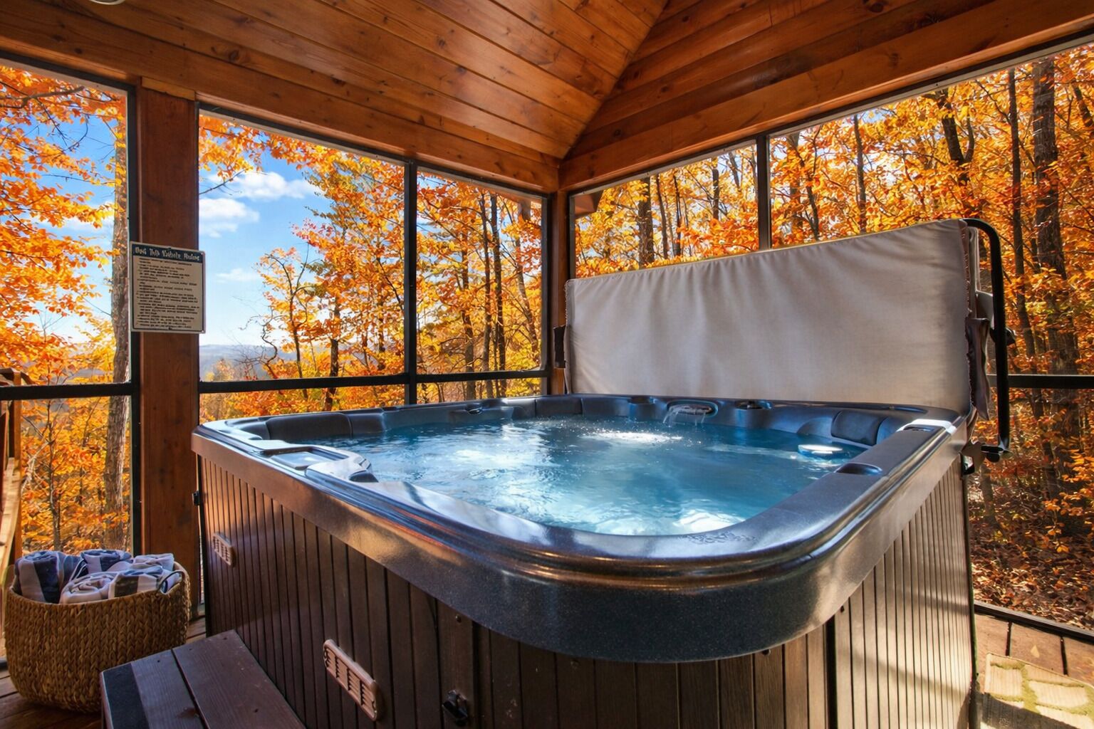 A hot tub in a wooden cabin with a view of autumn trees.