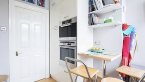 Cucina compatta con una porta bianca, un forno doppio e un piccolo tavolo con sedie.