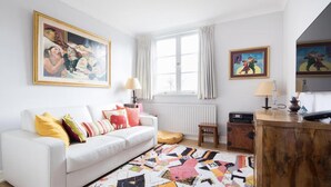 Un soggiorno con un divano bianco, cuscini colorati, un tappeto decorato e opere d'arte alle pareti.