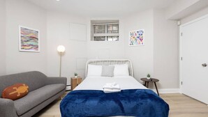 A modern bedroom with a bed, a grey sofa, and two side tables. - Petit Studio in Back Bay (Boston)