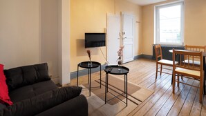 En stue med en sort sofa, et lille sort bord, et træspisebord med stole, et fjernsyn monteret på væggen og et vindue med udsigt.