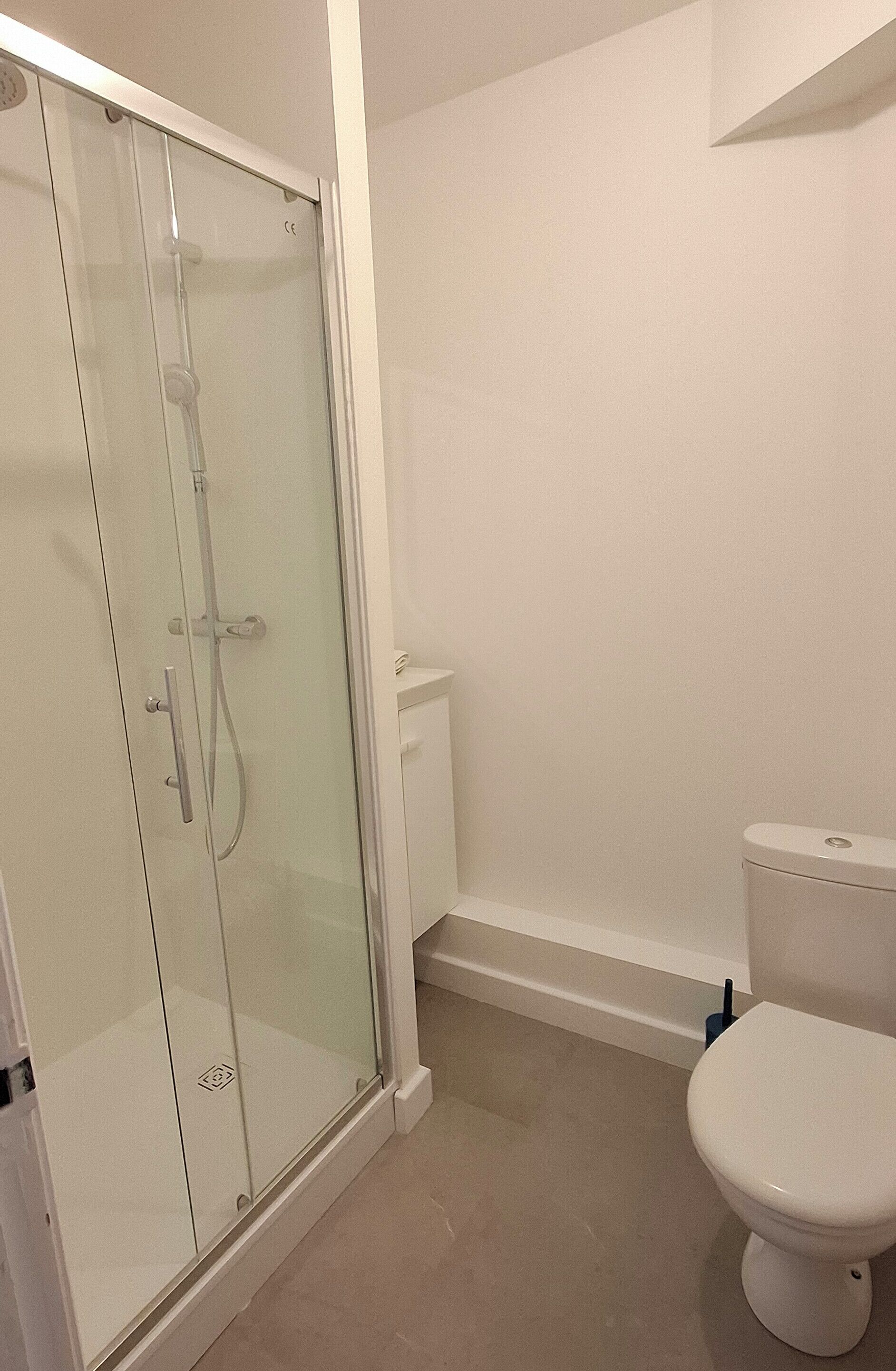 Un baño con cabina de ducha de vidrio, inodoro y lavabo blanco.