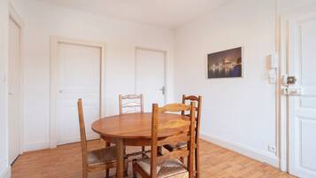 A dining area with a round wooden table and four chairs, white walls, and a ceiling light.